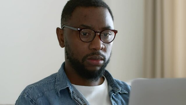 Remote work concept. Concentrated black man employee in glasses working online on laptop, reading e-mail, tracking shot