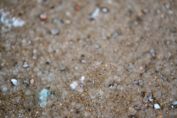 macro ground level closeup view of rock salt ice-melt on concrete with a frozen layer. 
