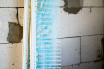 PVC window profile with cuff and mesh close-up at a construction site. Insulation and screed of window slopes