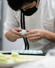 Obraz na płótnie Canvas Close up of asian male pastry chef making blue macarons. In the kitchen series.