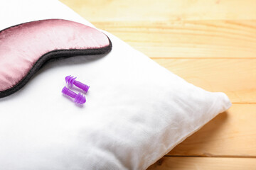 Earplugs, pillow and sleeping mask on wooden background