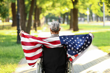 Young soldier in wheelchair with USA flag outdoors, back view
