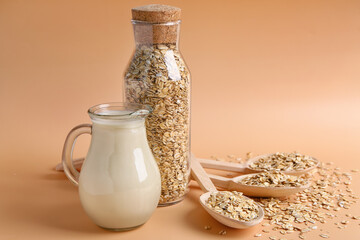 Spoons with raw oatmeal and jug of milk on color background
