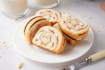 Plate with pieces of delicious sponge cake roll and milk on white table
