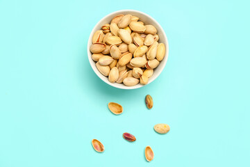 Bowl with tasty pistachio nuts on blue background
