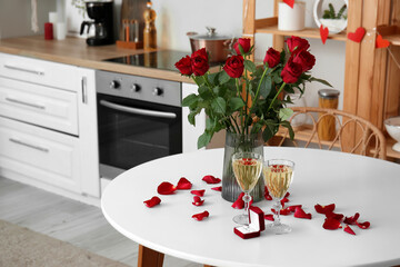 Engagement ring, vase with roses and glasses of champagne on dining table in kitchen decorated for Valentine's Day