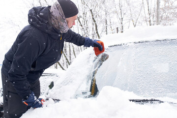 Fototapeta na wymiar Man cleans his car after a snowfall. Cleaning snow from windshield, Scraping ice, Winter car window cleaning