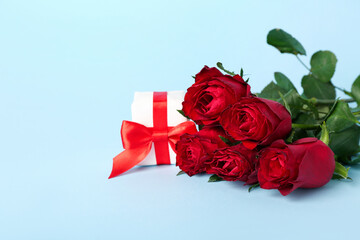 Red roses with gift on blue background. Valentine's Day celebration