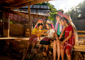Two of Asian girls and woman in Long Neck Karen Village enjoy to play with rock-paper-scissors game and other cheer up beside in basement of their house with warm light.