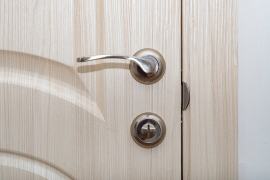 Close-up of a metal handle in a light wooden door in a modern style.