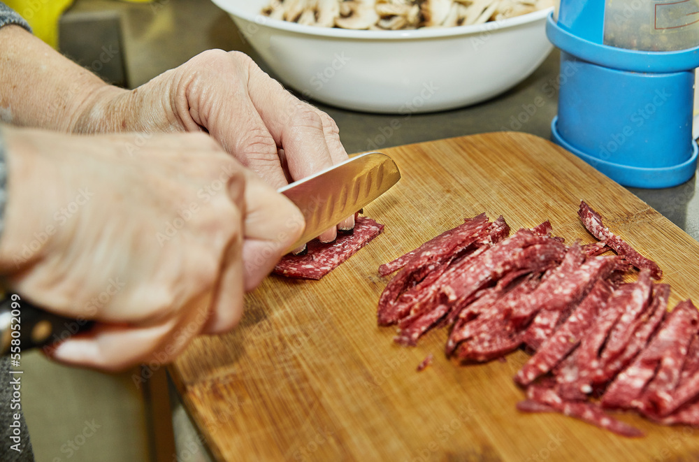 Poster Chef cuts salami on wooden board in the kitchen