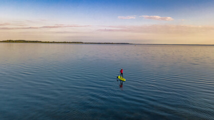Woman paddling on SUP board on beautiful lake aerial drone view with reflections from above....