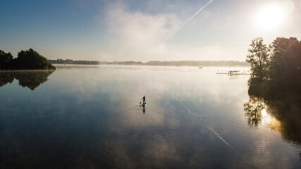 Woman paddling on SUP board on beautiful lake aerial drone view with reflections from above....