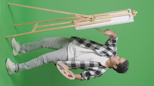 Full Body Of Asian Male Artist Painting On Canvas By Oil Paints And Brush In The Green Screen Studio
