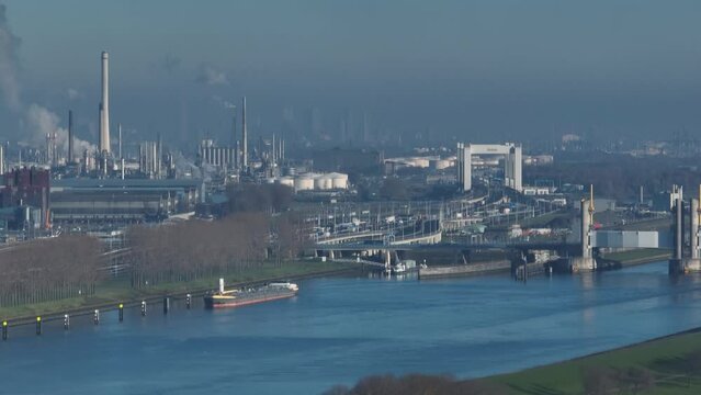 Aerial view of dense industrial center and oil refinery along a river outside the city of Rotterdam with the Botlek bridge and city in the background