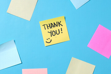 Top view of words thank you written on sticky note with colorful blank sticky notes for text space on blue background.  