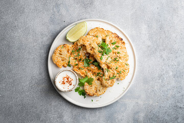 Cauliflower steaks with sauce on white plate, vegetarian dish, view from above