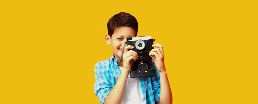 Portrait of happy little boy child with film camera on yellow background