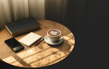 Close up view, Latte coffee in white cup with old book and smart phone on wooden table near the...