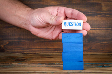 Question concept. Colorful blocks and a man's hand on a wooden texture background
