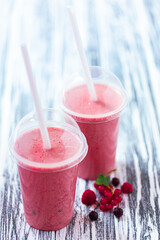 Two berries milkshakes in plastic cups with straws with ingredients on wood background. Vegan food