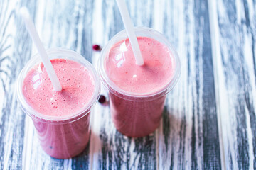Top down view of two berries milkshakes in plastic cups with straws on wooden table. Selective focus