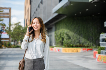 Fototapeta premium Asian business female calling on smart mobile phone and walking on street outside office building, Happy businesswoman talking on smartphone outdoor in city with client, business communication