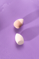 Two makeup sponges to apply foundation on a purple background