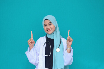 Smiling happy beautiful Asian Muslim woman doctor pointing above with finger 