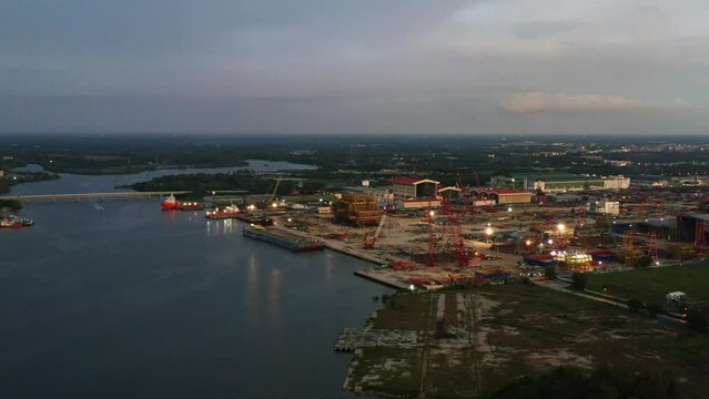 Aerial tracking shot capturing massive fabrication yard, plant and marine shipyard at Kampung Acheh Lumut port industrial park, ship building and repair hangars and hardstands, Perak, Malaysia.