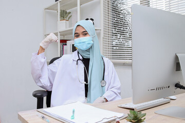 Fototapeta premium Young muslim woman with doctor gown and protective mask showing strong gesture at clinic