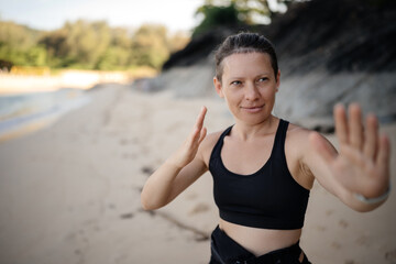 Portrait of a female athlete holding her hands in a defense or attack pose on the beach in the morning.