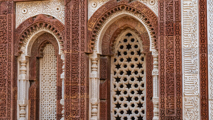 Fototapeta na wymiar The ancient temple complex of Qutub Minar. Details. The facade is made of red sandstone and white marble decorated with carved ornaments. The arched windows have decorative stone grilles. India. Delhi