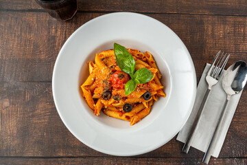 Penne pasta in tomato sauce, tomatoes decorated with parsley on a wooden background