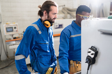 Handsome caucasian and African American carpenter man in safety blue uniform control machine of monitor button at factory	