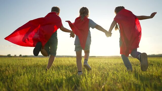 Group of children dressed as superhero. Children play in the park. Kid together in the summer in nature. Family in red suits is a childhood dream. Joyful funny kid play on the green grass in meadow.