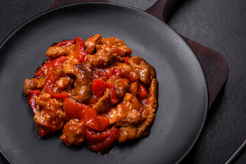 .Delicious juicy meat with hot peppers and sauce on a black ceramic plate