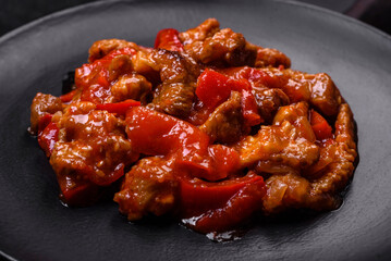 .Delicious juicy meat with hot peppers and sauce on a black ceramic plate