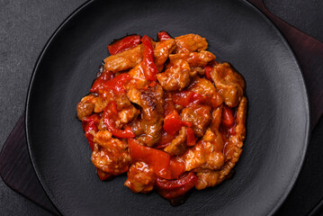.Delicious juicy meat with hot peppers and sauce on a black ceramic plate