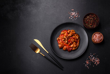 .Delicious juicy meat with hot peppers and sauce on a black ceramic plate