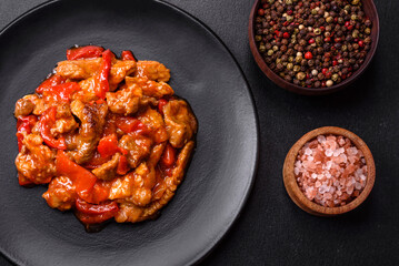 .Delicious juicy meat with hot peppers and sauce on a black ceramic plate