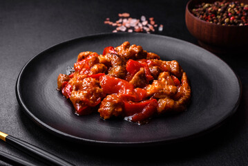 .Delicious juicy meat with hot peppers and sauce on a black ceramic plate