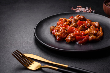 .Delicious juicy meat with hot peppers and sauce on a black ceramic plate