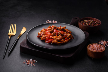 .Delicious juicy meat with hot peppers and sauce on a black ceramic plate