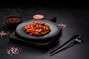 .Delicious juicy meat with hot peppers and sauce on a black ceramic plate