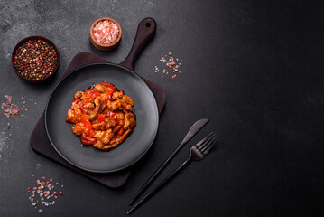 .Delicious juicy meat with hot peppers and sauce on a black ceramic plate