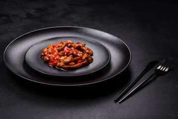 .Delicious juicy meat with hot peppers and sauce on a black ceramic plate