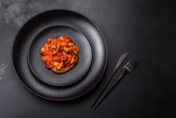.Delicious juicy meat with hot peppers and sauce on a black ceramic plate