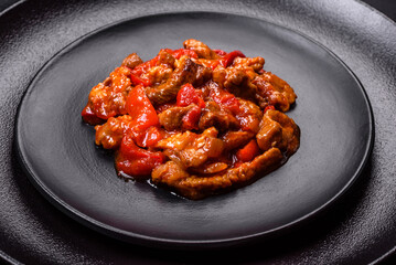 .Delicious juicy meat with hot peppers and sauce on a black ceramic plate