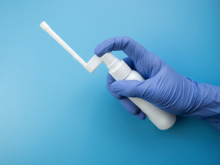 The doctor holds in his hands a spray for the treatment of the throat and nose on a blue...